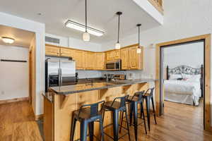 Kitchen with appliances with stainless steel finishes, a breakfast bar, light hardwood / wood-style flooring, and kitchen peninsula