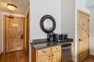 Kitchen featuring a textured ceiling, light brown cabinets, refrigerator, dark stone countertops, and dark hardwood / wood-style flooring