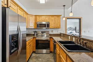 Kitchen featuring appliances with stainless steel finishes, hanging light fixtures, dark stone counters, and sink