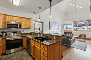 Kitchen with dark stone countertops, appliances with stainless steel finishes, hanging light fixtures, kitchen peninsula, and sink