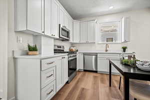 Kitchen with sink, white cabinetry, light hardwood / wood-style flooring, a textured ceiling, and stainless steel appliances