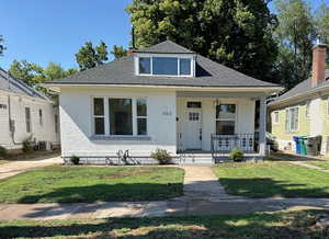 Bungalow featuring a porch, brick siding, a shingled roof, and a front yard