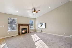 Living room featuring lofted ceiling, light colored carpet, a tiled fireplace, and ceiling fan