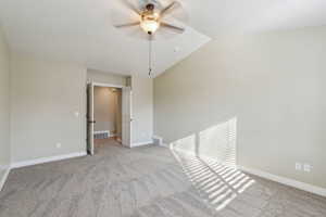 Spare room featuring ceiling fan, vaulted ceiling, and light colored carpet