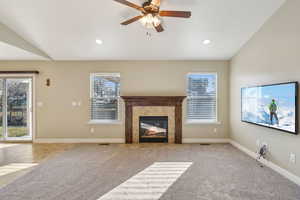 Unfurnished living room featuring a tile fireplace, light colored carpet, vaulted ceiling, and plenty of natural light