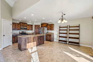 Kitchen featuring stainless steel appliances, sink, decorative light fixtures, an inviting chandelier, and a kitchen island with sink