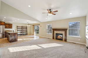 Unfurnished living room with sink, a tiled fireplace, ceiling fan with notable chandelier, and light carpet