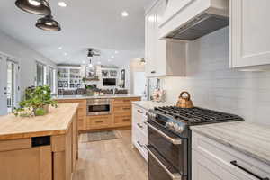 Kitchen featuring wooden counters, range with two ovens, lofted ceiling, wall chimney range hood, and backsplash