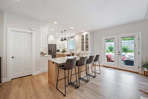 Kitchen featuring white cabinetry, a center island, light wood-type flooring, hanging light fixtures, and high end refrigerator