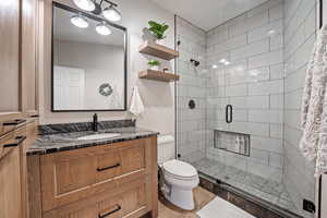 Bathroom with hardwood / wood-style floors, toilet, a shower with shower door, and vanity