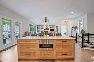 Kitchen featuring light stone counters, light hardwood / wood-style flooring, lofted ceiling, ceiling fan, and a stone fireplace