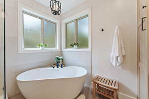 Bathroom with hardwood / wood-style floors, a notable chandelier, a tub to relax in, and plenty of natural light