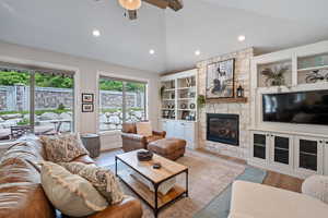 Living room featuring lofted ceiling, ceiling fan, light hardwood / wood-style flooring, and a stone fireplace