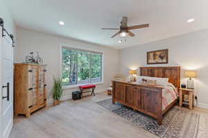 Bedroom with ceiling fan, light hardwood / wood-style flooring, and a barn door