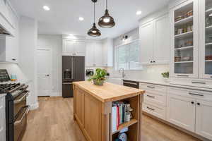 Kitchen with stainless steel appliances, white cabinetry, and hanging light fixtures