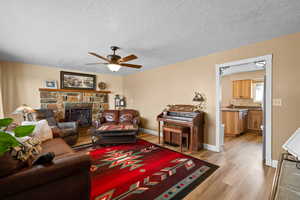 Living room featuring ceiling fan, light hardwood / wood-style flooring, a textured ceiling, and a fireplace