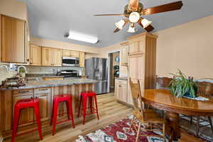 Kitchen with appliances with stainless steel finishes, light wood-type flooring, light brown cabinetry, decorative backsplash, and sink