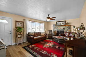 Living room featuring ceiling fan, light hardwood / wood-style flooring, a textured ceiling, and a fireplace