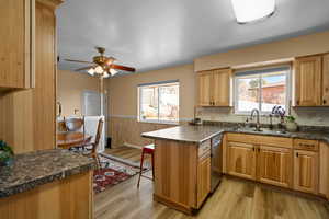 Kitchen with kitchen peninsula, stainless steel dishwasher, light hardwood / wood-style floors, ceiling fan, and sink