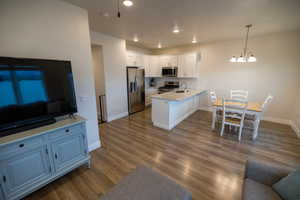 Kitchen featuring stainless steel appliances, kitchen peninsula, a notable chandelier, white cabinetry, and backsplash