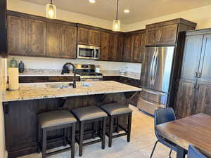 Kitchen featuring stainless steel appliances, sink, hanging light fixtures, and light stone countertops