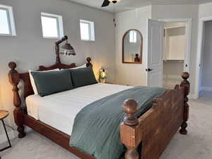 Bedroom with a walk in closet, light colored carpet, ceiling fan, and a closet