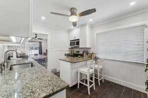 Kitchen with kitchen peninsula, stone counters, stainless steel appliances, sink, and white cabinetry