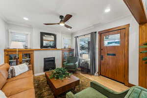 Family room with a fireplace, hardwood / wood-style floors, ceiling fan, and crown molding