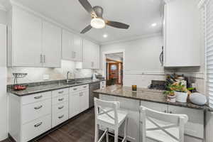 Kitchen with white cabinetry, sink, dishwasher, dark stone counters, and a breakfast bar