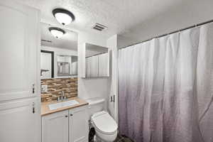 Bathroom with toilet, a textured ceiling, tub/shower, decorative backsplash, and vanity