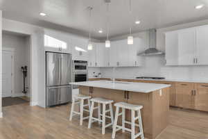 Kitchen featuring appliances with stainless steel finishes, sink, wall chimney range hood, white cabinetry, and an island with sink