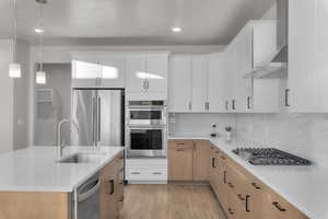 Kitchen with stainless steel appliances, white cabinetry, wall chimney exhaust hood, and sink