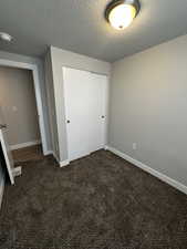 Unfurnished bedroom featuring a textured ceiling, a closet, and dark colored carpet