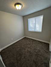 Unfurnished room featuring a textured ceiling and dark colored carpet