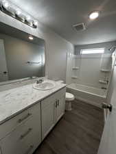 Full bathroom featuring washtub / shower combination, toilet, wood-type flooring, vanity, and a textured ceiling