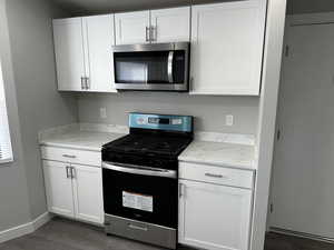 Kitchen with appliances with stainless steel finishes, dark wood-type flooring, white cabinetry, and light stone counters