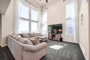 Living room featuring dark carpet, ceiling fan, and a wealth of natural light