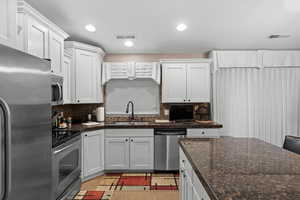 Kitchen with decorative backsplash, appliances with stainless steel finishes, white cabinetry, and sink