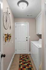 Laundry room with cabinets, a textured ceiling, separate washer and dryer, and light tile patterned flooring