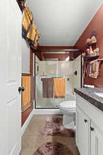 Bathroom featuring a textured ceiling, vanity, toilet, and a shower with shower door