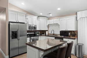 Kitchen featuring stainless steel appliances, sink, white cabinets, a center island, and lofted ceiling