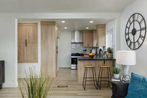 Kitchen featuring kitchen peninsula, stainless steel gas range oven,  exhaust hood, tasteful backsplash, and a kitchen bar