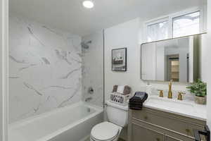 Full bathroom featuring toilet, vanity, a textured ceiling, and tiled shower / bath combo