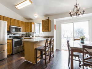 Kitchen featuring pendant lighting, a notable chandelier, lofted ceiling, a kitchen island, and appliances with stainless steel finishes