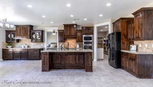 Kitchen with stainless steel appliances, tasteful backsplash, a kitchen island with sink, and dark brown cabinets