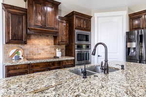 Kitchen featuring stainless steel appliances, light stone countertops, dark brown cabinets, and sink