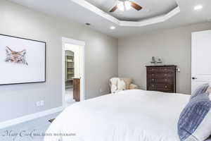 Carpeted bedroom featuring ceiling fan and a tray ceiling