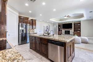 Kitchen featuring an island with sink, a raised ceiling, appliances with stainless steel finishes, ceiling fan, and sink