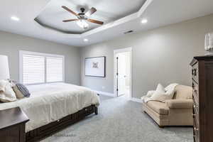 Bedroom featuring ceiling fan, light colored carpet, and a tray ceiling