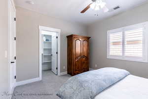 Bedroom featuring a walk in closet, ceiling fan, and light carpet